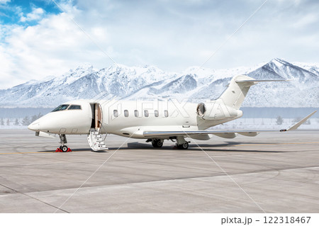 Modern white business jet with an opened gangway door at the winter airport apron on the background of high picturesque snow capped mountains 122318467