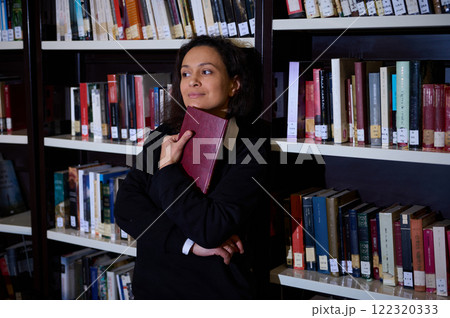 A woman in a library holding a book while standing near bookshelves, showcasing a serene and intellectual setting. 122320333