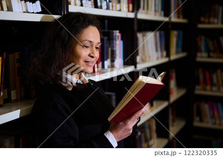 A woman is enjoying a book in a cozy library, surrounded by shelves of books. The scene highlights learning, personal exploration, and the tranquil atmosphere of reading in a library. 122320335
