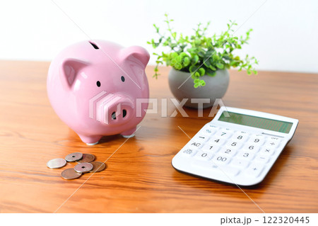 机に置かれた豚の貯金箱と電卓のイメージ 机に置かれた豚の貯金箱と電卓のイメージ 122320445