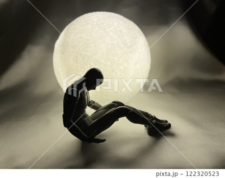 月を背にひざを抱えて落ち込む人形 122320523
