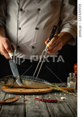 A skilled chef is filleting a fresh fish using a sharp knife while holding it steady with a fork. The chef's focused demeanor highlights the precision of the culinary art in a cozy kitchen 122320559