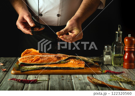 A skilled chef seasons a fresh salmon fillet with vibrant spices, blending rich colors and aromas in a rustic kitchen. The warm atmosphere highlights culinary creativity and tradition 122320560