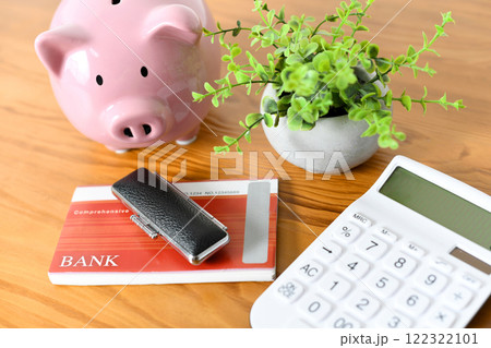 机に並んだ銀行通帳と印鑑と電卓と貯金箱 122322101