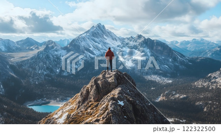 Hiker on Rocky Summit Overlooking Snow-Capped Mountain Peaks and Alpine Lake 122322500