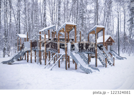 Children's playground is a town for playing in the winter forest. A snowy playground with vibrant slides and climbing structures, nestled in a magical winter wonderland. 122324081