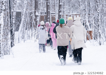 Children of different ages walk through the winter forest. A diverse group of people enthusiastically walking together along a snowy forest trail 122324082