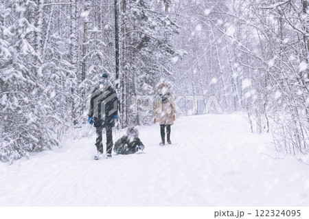 Family winter in the park in the forest. Dad mom and child on a sled walk in the woods in the snowfall. The faces are not visible because of the snowflakes. Winter Wonderland A Family Excitedly Enjoys 122324095