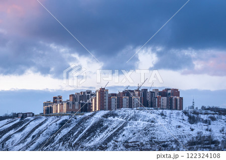 The new residential complex Akademgorodok in Krasnoyarsk, Russia, on a high bank in the winter evening. Contemporary Modern Buildings Resting on a Snowy Hilltop Beneath a Dramatic Sky Above 122324108
