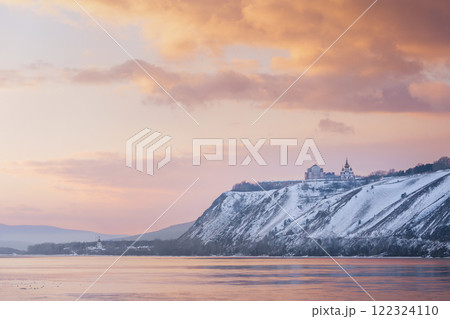 Winter landscape - a Russian Orthodox church snow-covered high bank of the Yenisei River in Krasnoyarsk, Russia. Beautiful view of the Yenisei river at orange sunset 122324110