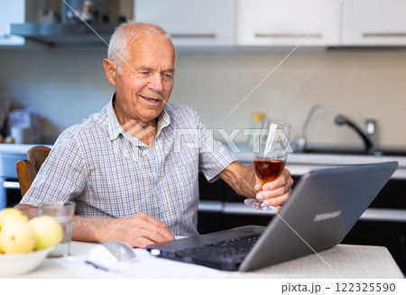 Elderly man with glass of cognac talking through internet 122325590