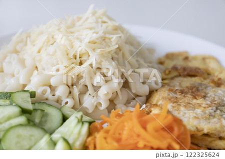 The pasta topped with cheese, fresh cucumbers and carrots, and pork chop in the eggs on the white plate The pasta topped with cheese, fresh cucumbers and carrots, and pork chop in the eggs on the white plate 122325624
