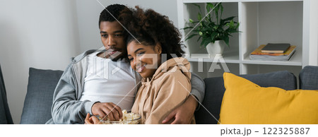 Banner African American couple wife husband watching movie. Family pastime and leisure, watch television, rest. Relaxed man and woman watching TV series together sitting on couch at home enjoying Banner African American couple wife husband watching movie. Family pastime and leisure, watch television, rest. Relaxed man and woman watching TV series together sitting on couch at home enjoying 122325887