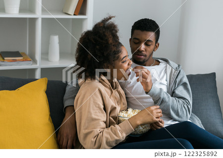 African American couple shares a playful and relaxed moment on the couch, with the man feeding popcorn to the woman. TV, series and streaming service concept 122325892