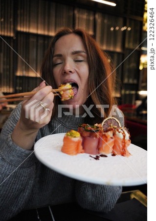 Woman Indulging in Gourmet Sushi with Chopsticks at a Chic Restaurant Woman Indulging in Gourmet Sushi with Chopsticks at a Chic Restaurant 122326464