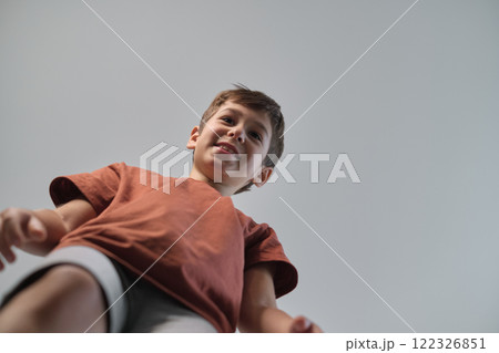 A smiling boy is captured from a low angle, creating a playful and engaging perspective. The image highlights joy, energy, and the curiosity of childhood. 122326851