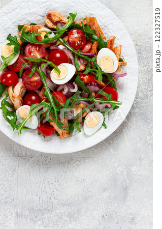a warm salad with fried chicken fillet, arugula and cherry tomatoes, and boiled quail eggs, on a white plate, no people. 122327519