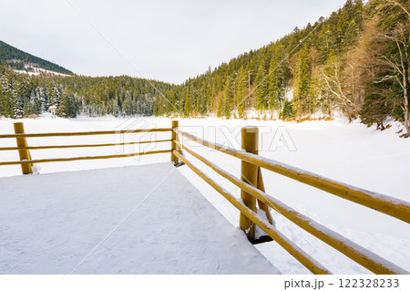 pier on the synevyr lake in winter. sunny weather. spruce forest. landscape of national park in carpathian mountains of ukraine. frozen and snow covered water surface. scenic view pier on the synevyr lake in winter. sunny weather. spruce forest. landscape of national park in carpathian mountains of ukraine. frozen and snow covered water surface. scenic view 122328233