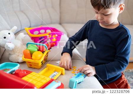 A boy is counting toy money while playing with a toy cash register. 122328706