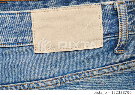 Close-up of blue denim jeans featuring an empty beige leather patch, detailed stitching, and a belt loop, ideal for branding, fashion, or textile-focused projects. 122328796