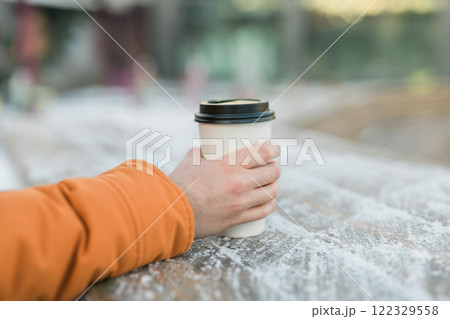 Hand holding a takeaway cup of hot coffee on a frosty wooden surface, copy space. Warm drink during wintertime 122329558