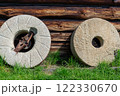Millstones against the wall of an old wooden house. 122330670
