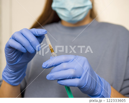 Medical professional wearing protective gear handling vaccine-loaded syringe, preparing immunization procedure with careful precision in clinical setting Medical professional wearing protective gear handling vaccine-loaded syringe, preparing immunization procedure with careful precision in clinical setting 122333605
