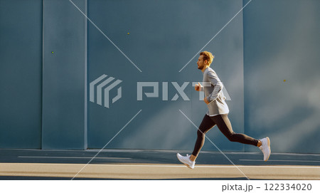 Man running on urban street in modern attire during bright day 122334020