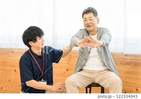 リハビリで体操をするシニア男性と理学療法士・作業療法士の男性スタッフ 122334843
