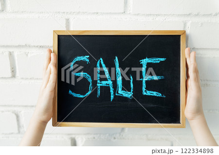Blue word Sale on black chalk board in children's hands on white brick wall 122334898