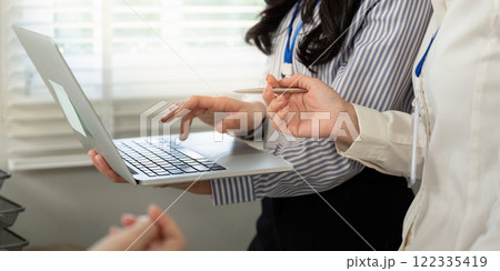 Diverse team collaborating on a laptop during a strategic discussion in a contemporary office setting Diverse team collaborating on a laptop during a strategic discussion in a contemporary office setting 122335419