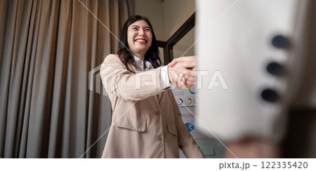 Joyful female professional smiling while shaking hands to finalize a business agreement in modern office Joyful female professional smiling while shaking hands to finalize a business agreement in modern office 122335420