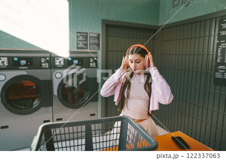 A Young Woman is Happily Enjoying Music While Relaxing in a Cozy Laundromat Space 122337063