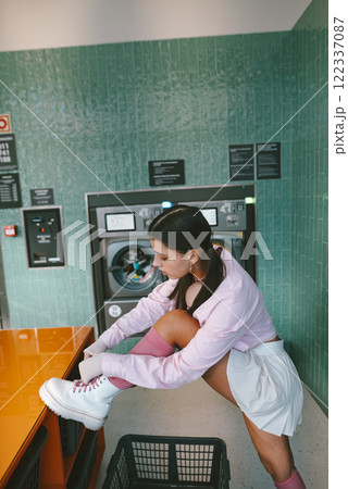 A young woman is tying her shoelaces in a chic and stylish laundry room environment 122337087