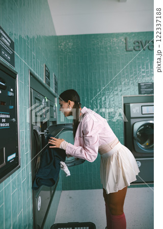 A young woman is engaged in the process of doing laundry in a modern, stylish laundromat A young woman is engaged in the process of doing laundry in a modern, stylish laundromat 122337188