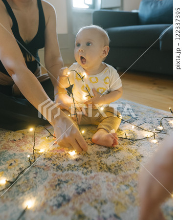 A Sweet Baby Joyfully Playing with Twinkling Christmas Lights in a Cozy Home Setting 122337395