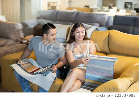 In exhibition hall,couple sat down on sand-colored sofa and keep sets of upholstery material samples 122337985