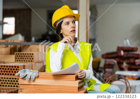 Woman foreman in a yellow vest and a protective helmet keeps track of bricks 122338123