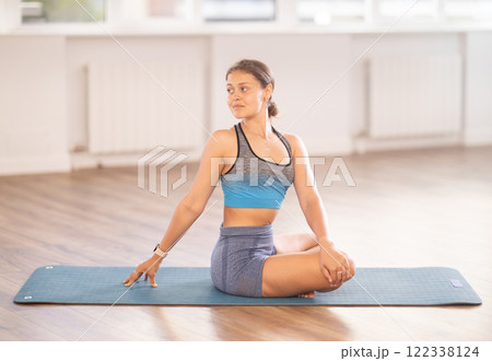 Young woman practicing parivritta sukhasana yoga pose 122338124