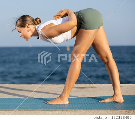 Athletic girl meditates in a yoga pose parshvottanasana on seashore 122338490