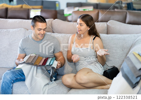 In store wife sit with legs on gray sofa to test in use,husband examines upholstery fabric In store wife sit with legs on gray sofa to test in use,husband examines upholstery fabric 122338521