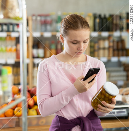 Checking expiration date of chips - female shopper scans QR code on label of jar canned olives using smartphone 122338560
