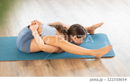 Sportive girl practicing complex pose of yoga in light room 122338654
