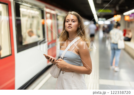 Young woman with phone stands at metro station 122338720