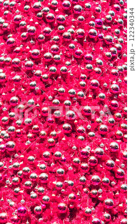 A vibrant close-up of metallic silver and magenta Christmas ornaments densely packed onto bright magenta tinsel, creating a festive and dynamic texture 122340344