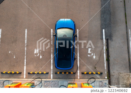 Top view of blue electric vehicle charges at a designated parking lot station 122340692