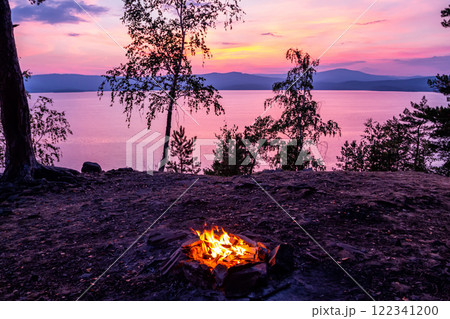 Campfire on the shore of a picturesque lake at sunset 122341200