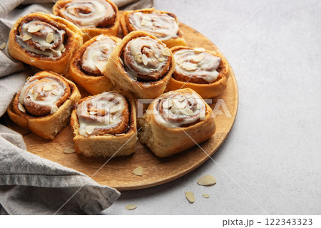 Delicious cinnamon rolls with white icing and almond flakes resting on wooden plate 122343323