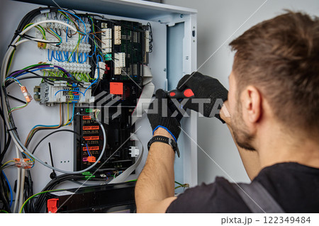 Technician working on internal wiring of heat pump, inspecting electrical connections. Specialist servicing heating and cooling system. Electrician with screwdriver tightening screws on control panel Technician working on internal wiring of heat pump, inspecting electrical connections. Specialist servicing heating and cooling system. Electrician with screwdriver tightening screws on control panel 122349484