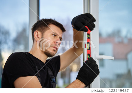 Professional builder using red spirit level for alignment of window frame during installation. Repairman adjusting white pvc windows. Concept of repair and home renovation 122349487